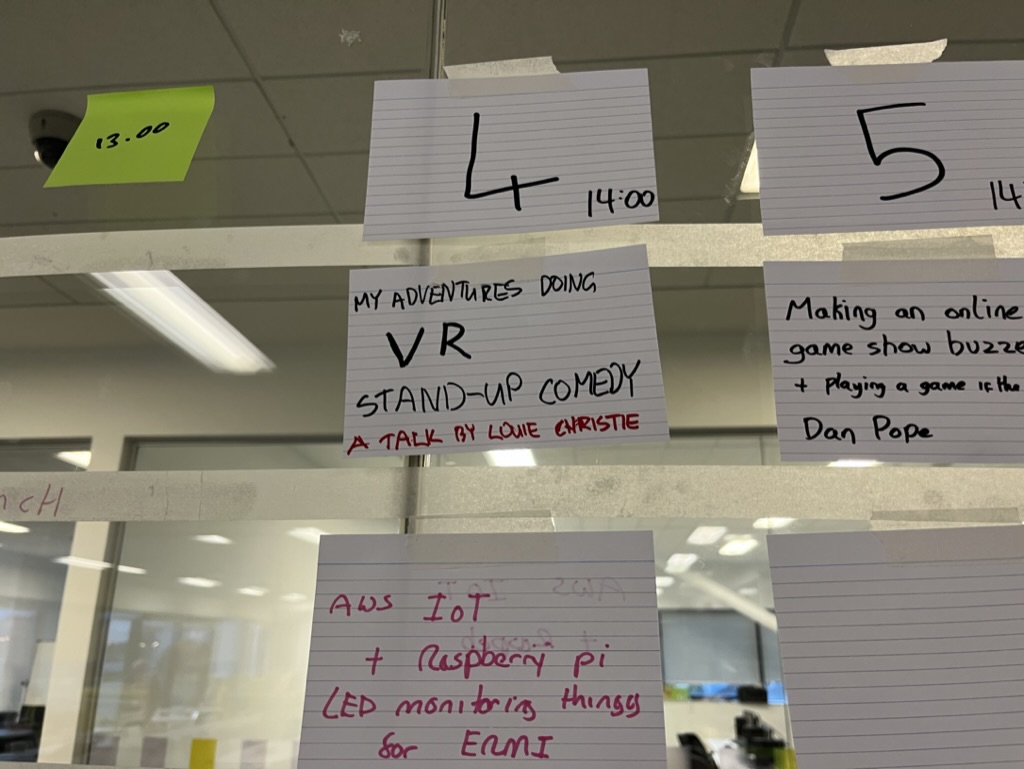 Post it note stuck on a board says 'My adventures doing VR stand-up comedy. A talk by Louie Christie'.